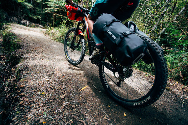 Person riding a bicycle with a black bag on a forest trail
