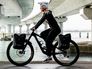 Woman riding a bike under a bridge with aeroe bags